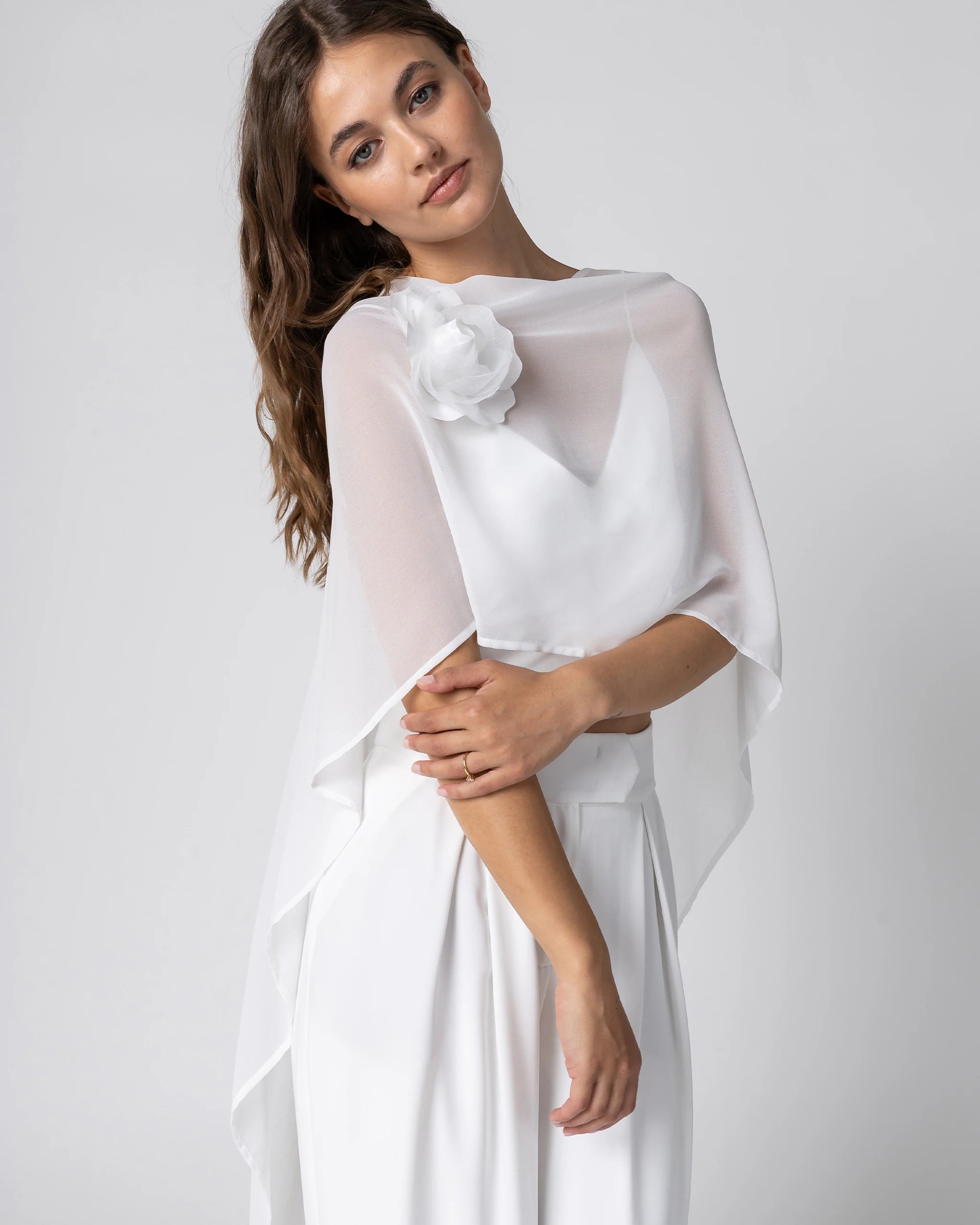 Braut in modernem Braut Jumpsuit mit Bralette Top, weiter Marlene Hose und Chiffon Cape mit Blütenbrosche