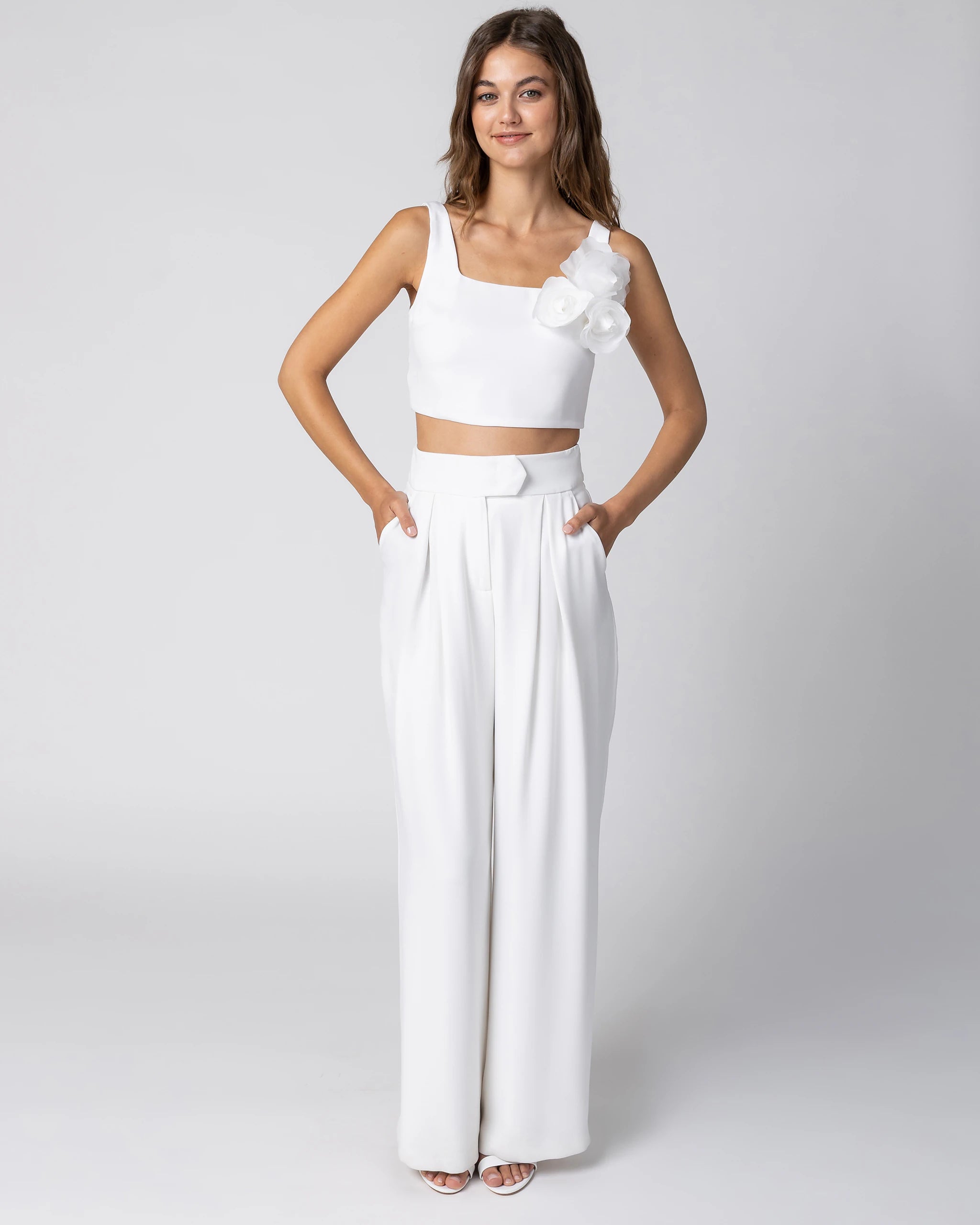 Braut in modernem Hosenanzug mit Crop Top, weiter Marlene Hose und Chiffonblume in Ivory Ansicht vorne