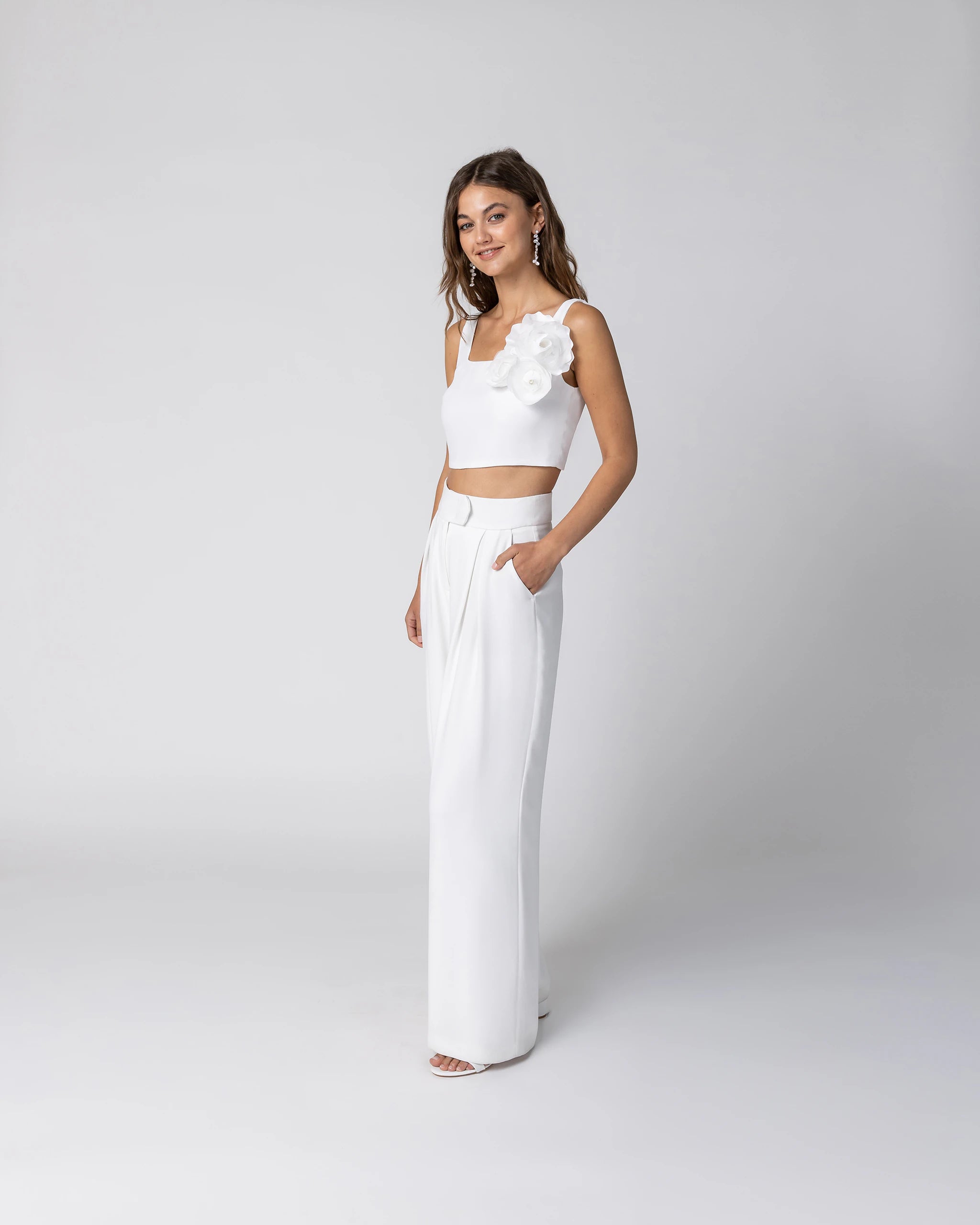 Braut in modernem Hosenanzug mit Crop Top, weiter Marlene Hose und Chiffonblume in Ivory Ansicht vorne